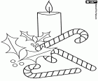 Candy canes, a lit candle and a sprig of holly with red berries
